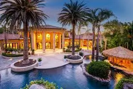 A stunning, well-lit luxury mansion with a large pool and palm trees, showcasing the high-end custom fencing and gate solutions Horizon Fence offers for prestigious properties throughout Granite Bay.