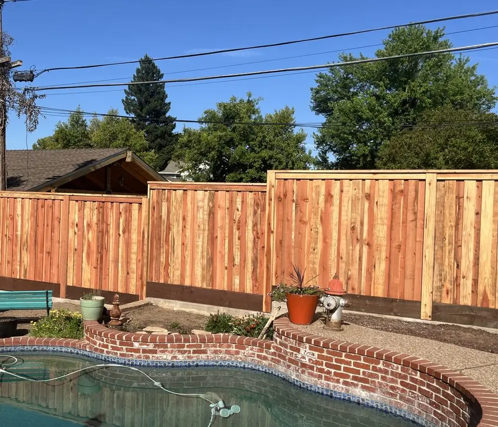 Newly installed vertical wood fence in a residential Orangevale backyard, serving as a safety barrier around a brick-edged swimming pool with landscaping in the foreground.