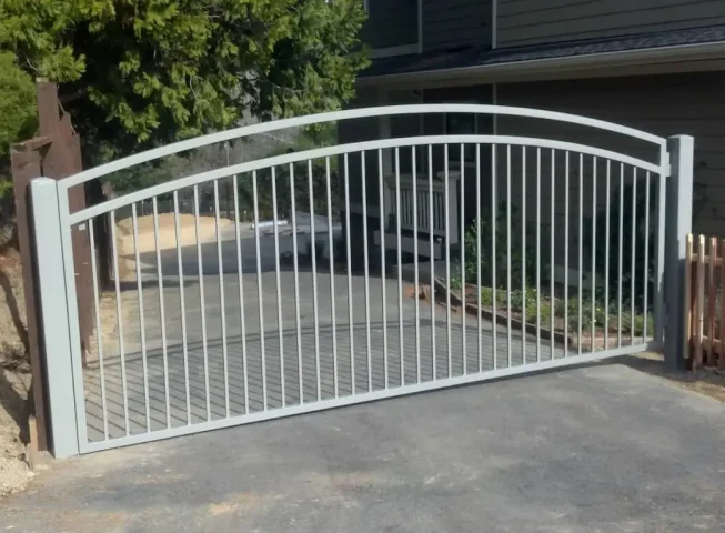 Arched iron driveway gate with vertical bars and light gray finish installed at a residential property in Roseville