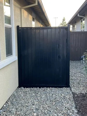 Black vinyl privacy fence installed between two residential homes in Roseville, creating a clean and modern barrier over decorative rock landscaping.