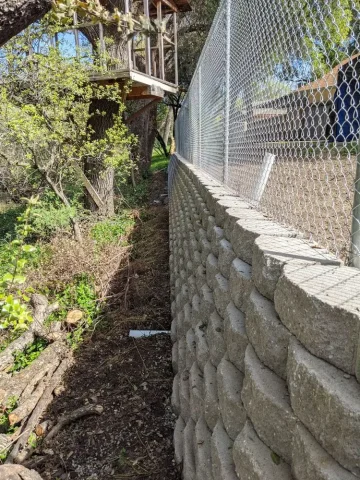 Chain link fence installed atop a stone retaining wall in a Rancho Cordova backyard, near a wooden treehouse structure, providing a sturdy safety barrier and property division.