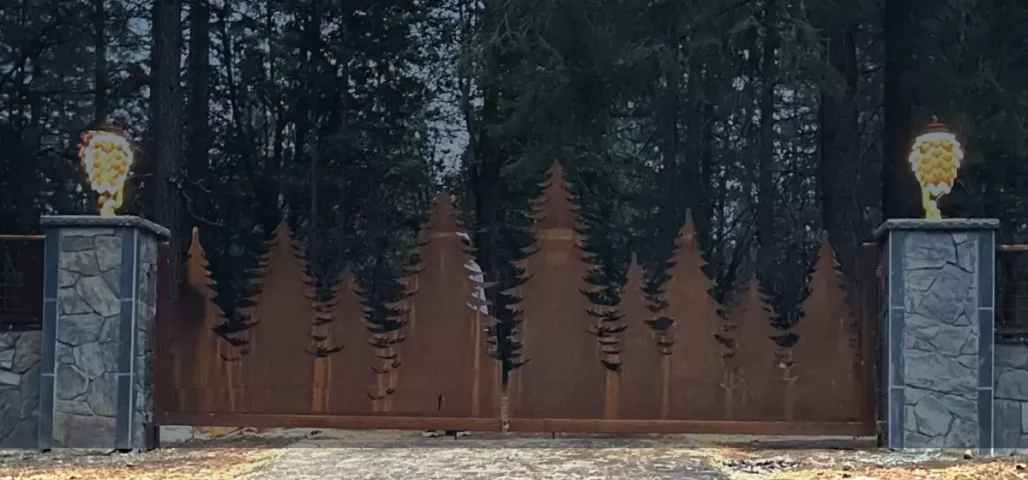 Custom metal driveway gate with forest tree design and stone columns, built by Horizon Fence & Custom Gates in Sacramento