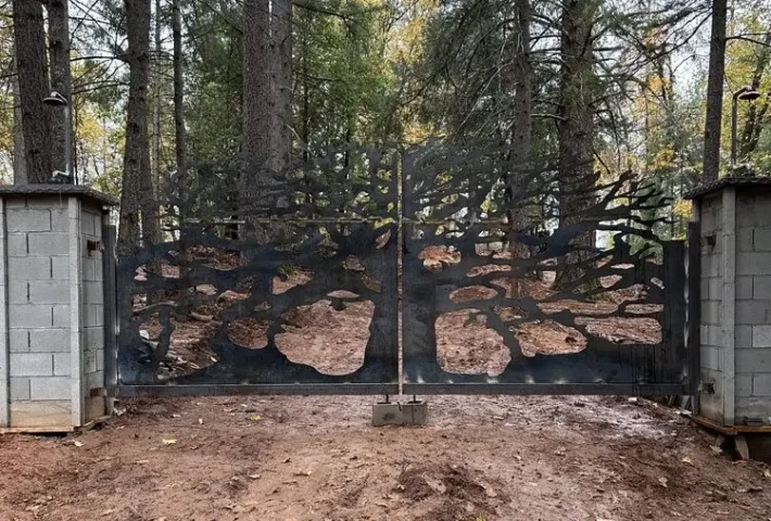 ustom driveway gate with artistic tree design cut into black metal panels, installed between concrete block pillars in Granite Bay