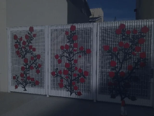 White metal gate with artistic floral design featuring black branches and red circular flowers, providing a decorative and secure entrance in Sacramento.