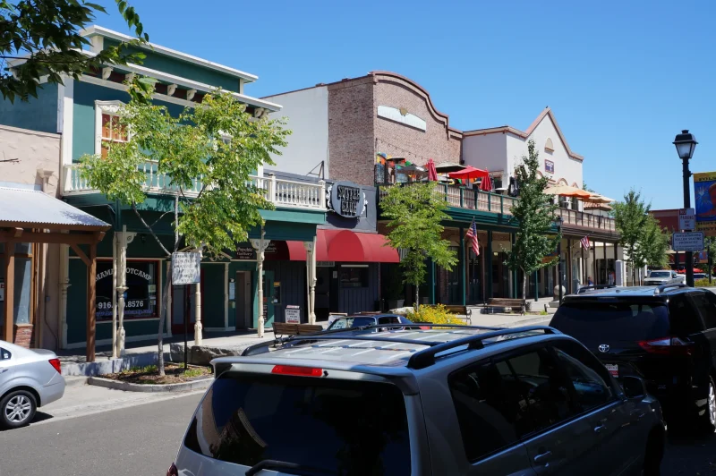 Colorful historic buildings and shops along Sutter Street in Folsom, California, with parked cars and trees lining the street.