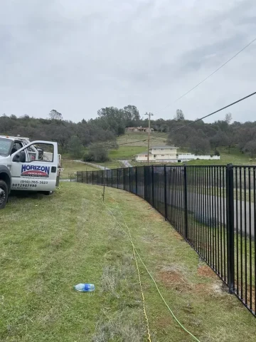 Black iron and ornamental fence installed along a grassy property slope in El Dorado Hills, with Horizon Fence & Custom Gates, Inc. truck parked nearby