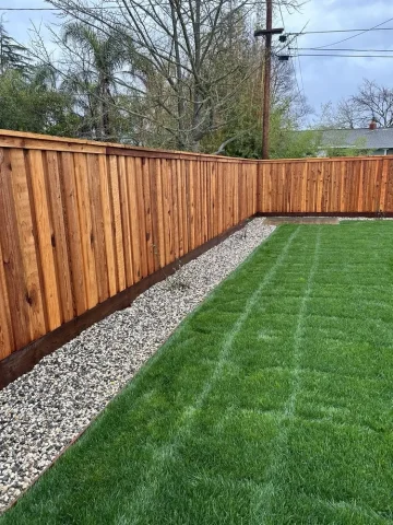 Freshly installed vertical wood fence surrounding a residential backyard in Orangevale, bordered with decorative gravel and lush green grass.