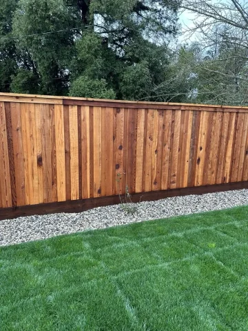 Tall wooden privacy fence with vertical planks installed in a well-maintained backyard in Orangevale, bordered with gravel and lush green grass.